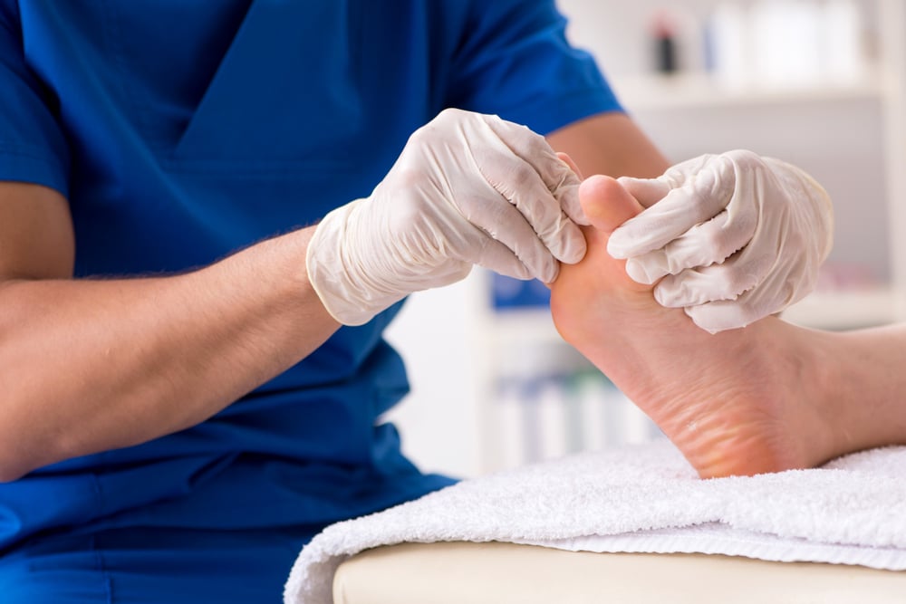 Podiatrist holds a man’s bare foot, closely examining his swollen big toe joint.