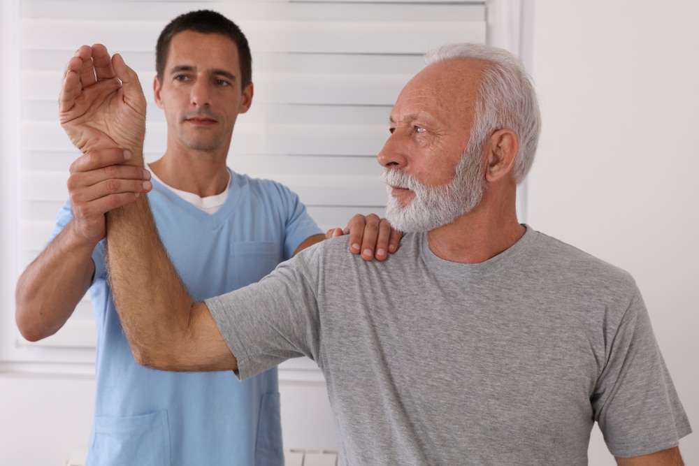 Physical therapist working with senior man dealing with arthritic pain in shoulder.