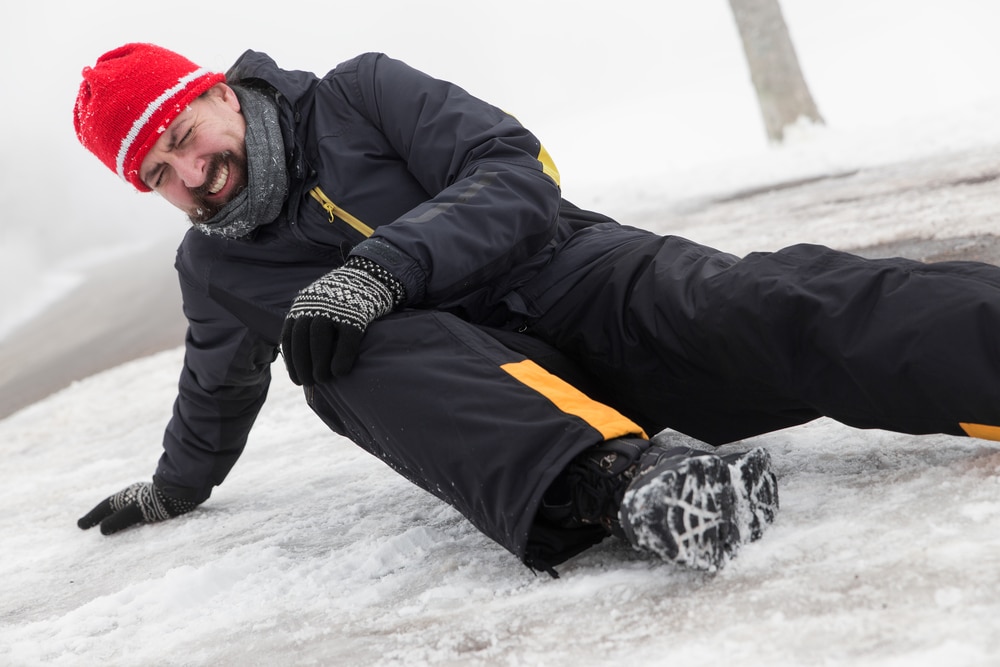 Man on ground holding his knee after slipping on icy driveway.