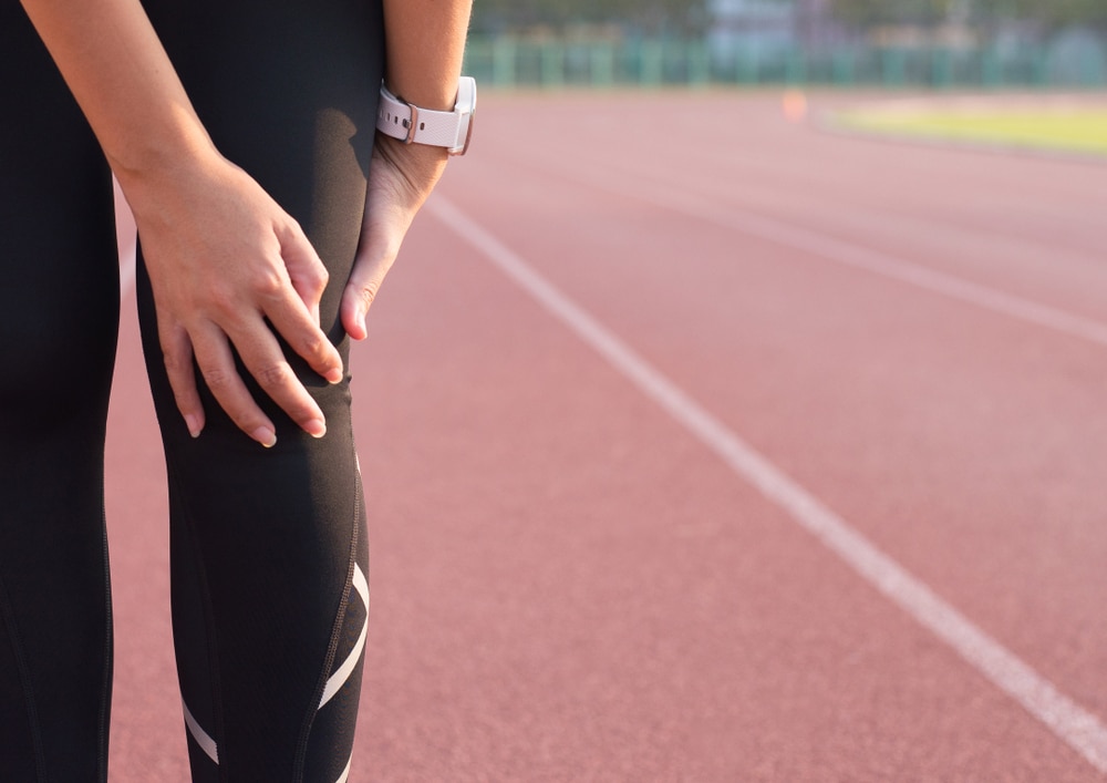 Woman holding her knee after tearing acl running on outdoor track.