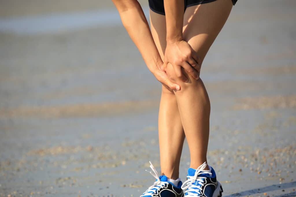 Woman holding knee in pain, possibly from acute injury or a chronic condition.