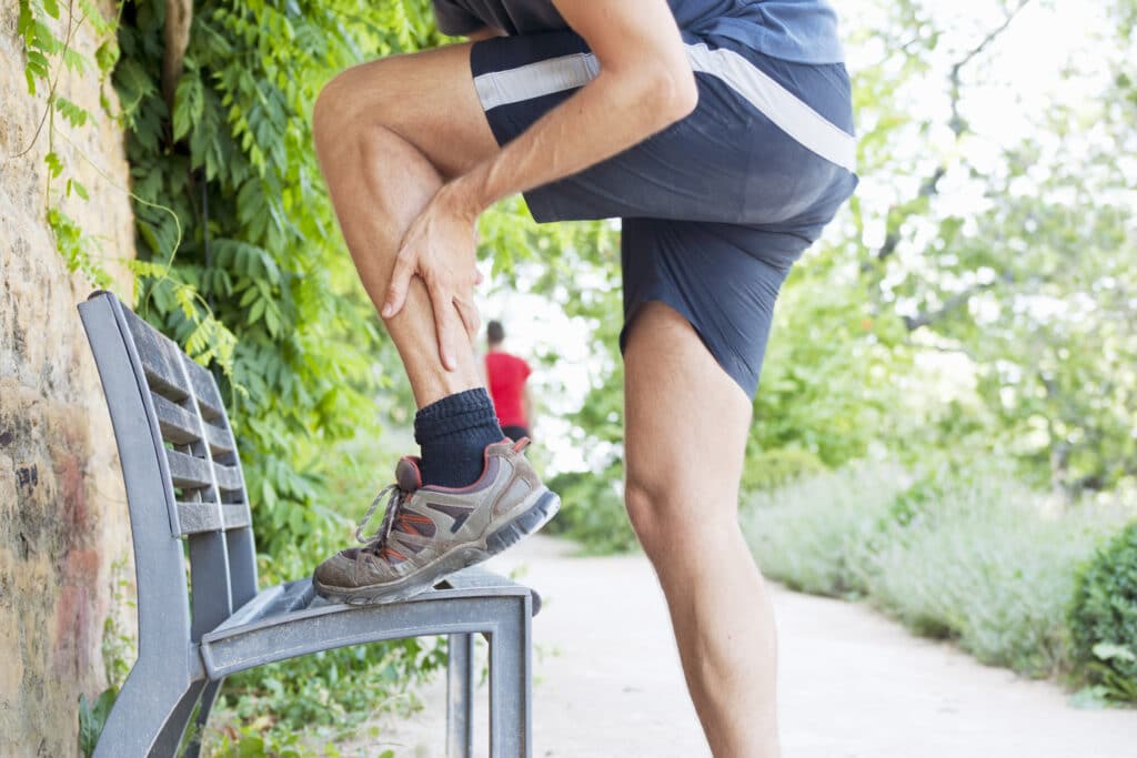 Man outside who was on a run, holding his injured ankle in pain