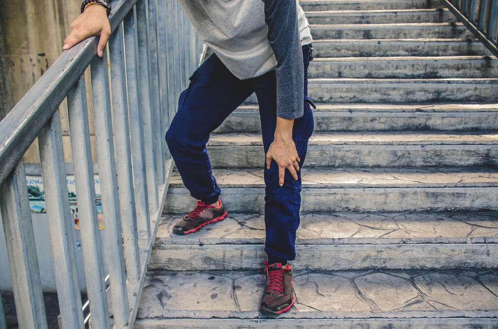 Person holding their knee while using stairs, representing knee pain when going up or down steps.