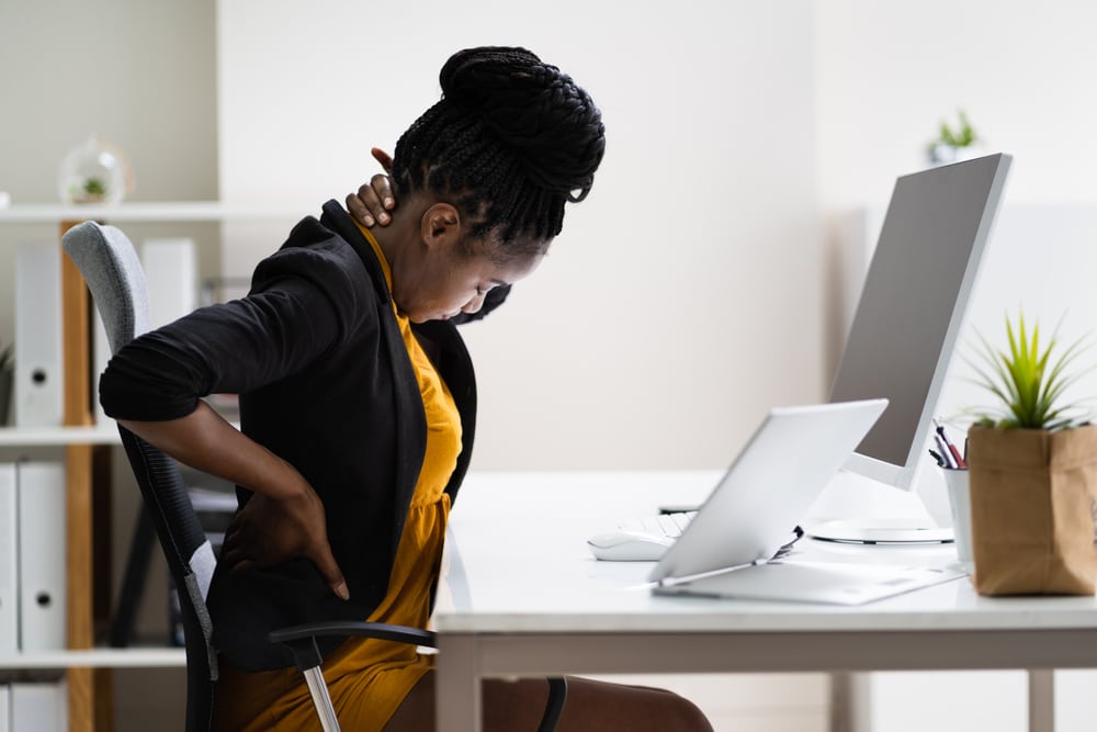Woman at a desk holding her neck and lower back, representing neck pain that may require orthopedic evaluation.