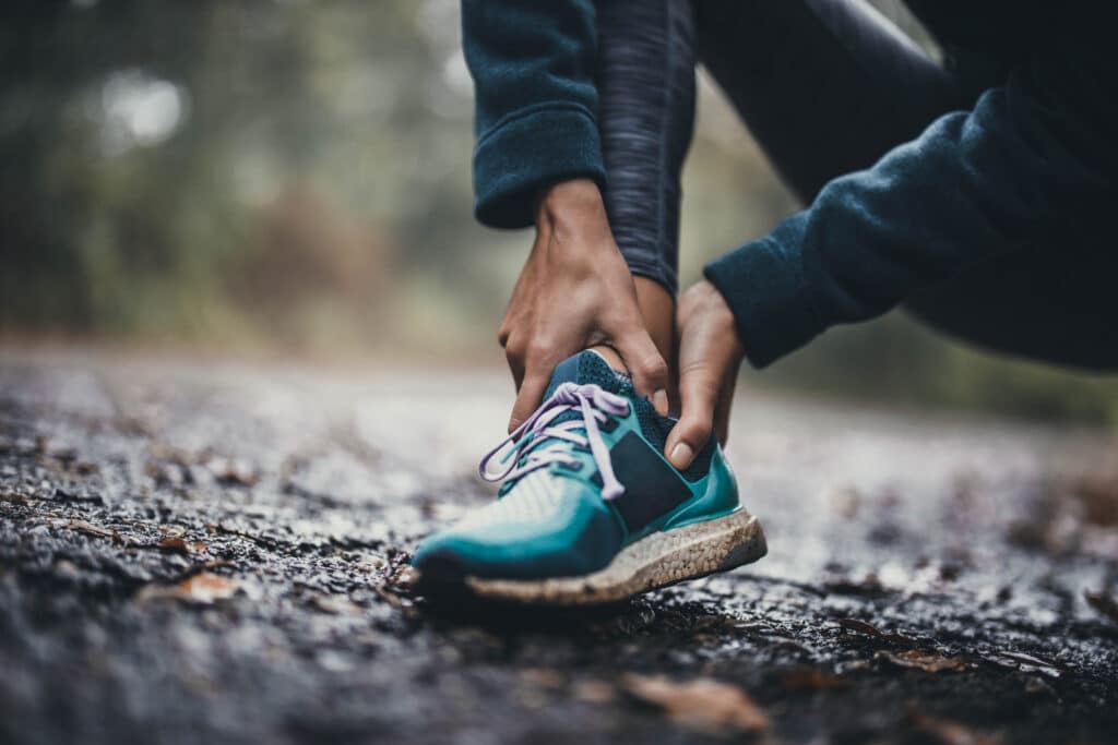 Person holding the back of their ankle while experiencing Achilles tendon pain outdoors.